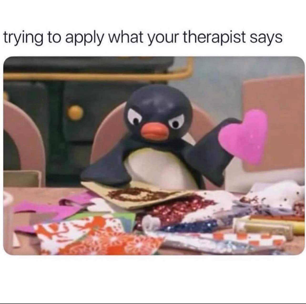 The meme features a penguin character from the children's TV show "Pingu" sitting at a table surrounded by papers and art supplies. The text above the image reads "trying to apply what your therapist says" and the penguin is holding up a paper heart with a scowl on its face, implying frustration with the process of applying therapy advice. The image is humorous because it pokes fun at the often-challenging process of putting into practice the advice and guidance of a therapist.